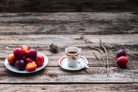 Cup of coffee and fresh plums on wood, free space. Warming drink with tasty fruit on old rustic wooden background, copy space for textの写真素材