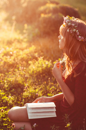 Profile of girl in wreath with book, sun flare effect. Free space on green meadow, attractive woman...