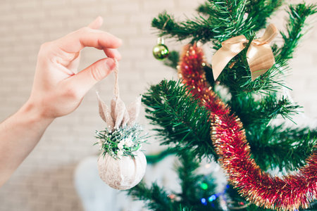 Christmas tree decorating with sparkling toy. Hand holding beautiful white decorative ball near pine tree with tinsel.の写真素材