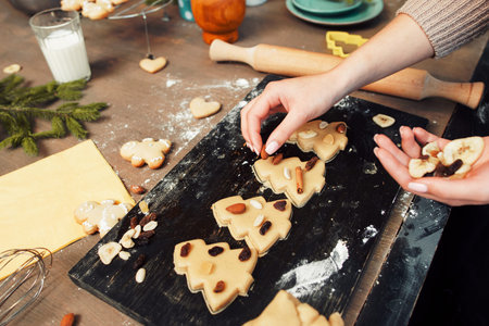 Woman decorating cookies with nuts and dried fruits. Top view on confectioner workplace while...