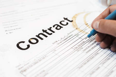 Dirty contract papers with cracker and coffee trace. Close-up of business documents of busy and tired businessman hand signing it. Mess on workplaceの写真素材