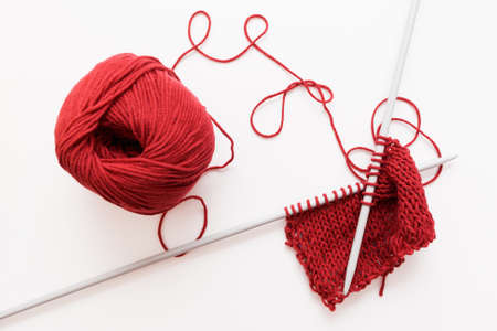 Red woolen thread and knitting needle isolated on white background. Sample of bordo knitted cloth with worktools. Handiwork, leisure, hobby conceptの写真素材