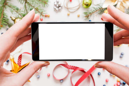 Taking Christmas picture on smartphone, mockup. Woman holding mobile phone and making photography, New year trumpery frame. Hobby, network conceptの写真素材