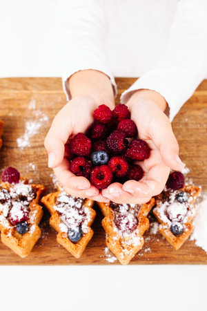 Child holding full palms of fresh berries, flat lay. Top view on kid hands with tasty raspberries...