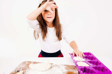 Tired girl with floured hands on kitchen. Little confectioner forming cakes, free space on white background. Homemade bakery, children culinary, pastry making conceptの写真素材