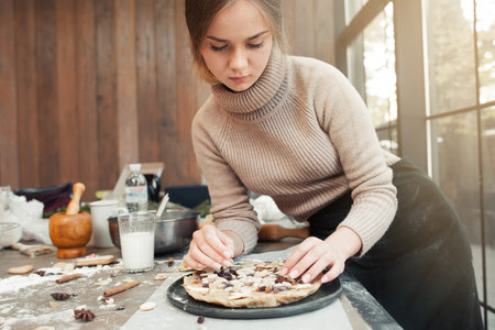 Woman decorating pie with dried fruits, free space on wooden background. Culinary classes, pastry...
