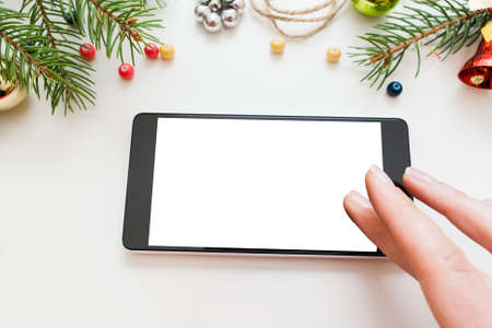 Woman using smartphone, Christmas frame, mockup. Female hand touching blank screen of mobile phone, white background with xmas tree borderの写真素材