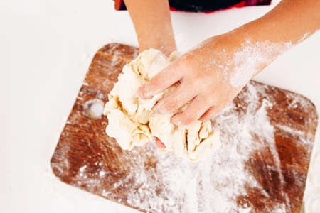 Kid hands with dough close-up. Top view on little baker kneading raw pastry above wooden cutting board. Homemade bakery, children culinary, sweets making conceptの写真素材
