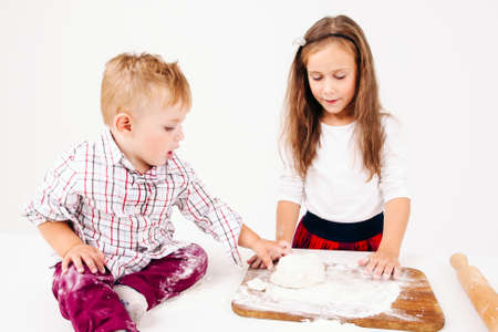 Little boy touching raw dough near sister. Little girl cooking bakery on kitchen, her brother help her, free space on whiteの写真素材