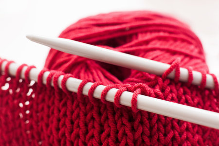 Knitting needles and bordo ball of yarn on white background. Close-up of handmade knitted cloth with tools. Handiwork, leisure, hobby conceptの写真素材