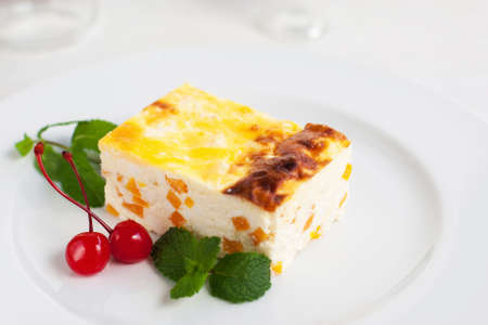 Cheesecake with pumpkin served with mint and cherry. Gentle dessert on white plate, free space. Homemade bakery conceptの写真素材