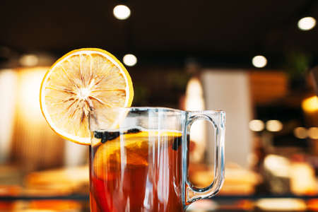 Cup of hot tea with orange at bar close-up. Glass with sweet winter drink at restaurant, blurred cafe background. Warming winter beverageの写真素材