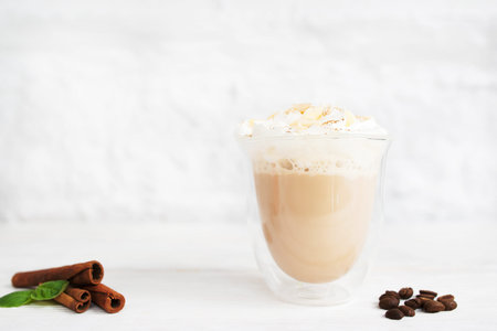 Glass of latte with cinnamon sticks and coffee beans. Cup of creamy cappuccino on white background, free space for text or advertisementの写真素材