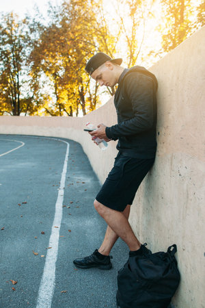Sportsman using smartphone on training, free space. Side view on young man chatting or networking...