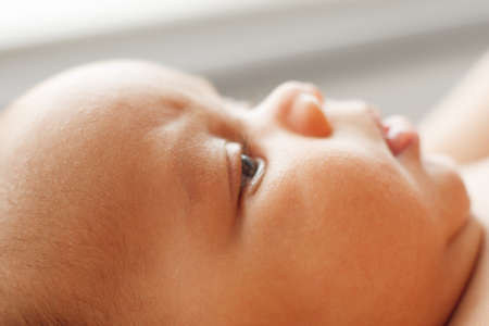 Close-up of newborn baby face, adorable child. Portrait of tranquil little kid looking up. Childhood, innocence, infant conceptの写真素材