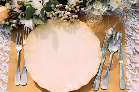 Empty plate with silverware on table, void. Restaurant serving for banquet, wedding, celebration or dinner event with flower decoration, flat layの写真素材