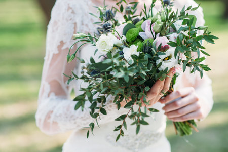 Green autumn wedding bouquet in bride hands. Unrecognizable woman in wedding dress holding flowers. Celebration, love, event in rustic style conceptの写真素材