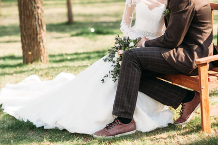 Bride and groom sitting on bench in park, free space. Happy just married couple having rest outside. Love, relax, care, fashion, family conceptの写真素材