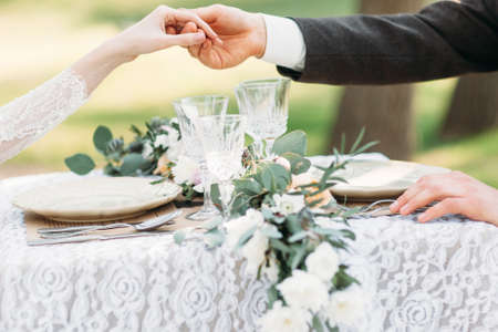 Couple holding hands above served table. Groom help his bride to stand up. Love, etiquette, care conceptの写真素材