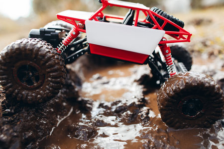 Toy suv riding through mud, side view. Small crawler overcoming dirty road in countryside, close-up....