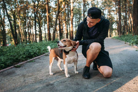 Young man playing with his dog in forest. Evening walk with pet on nature. Healthy lifestyle, domestic animal, nature conceptの写真素材