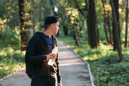 Young man looking back on forest road, free space. Young tourist having break for drinking water. Standing with bottle guy in wood.の写真素材