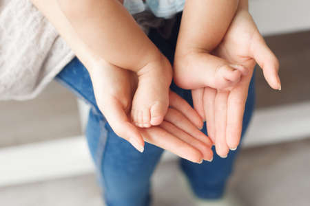 Tiny newborn baby legs on female hands, close-up. Mother holding her kid feet in shape of lovely heart. Love, care, happy family conceptの写真素材