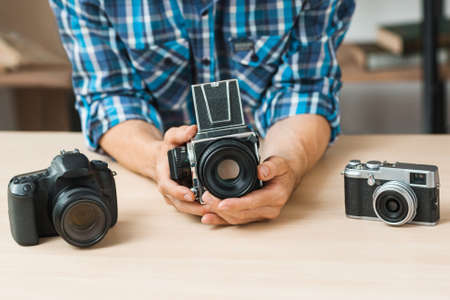 Man holding old photo camera in hands. Blogger compare different generations of photographing equipment. Technology progress conceptの写真素材