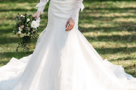Bride in beautiful dress walks with bouquet on grass. Close-up of white wedding dress, free space....