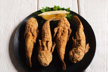 Tasty fried fish on black plate. Top view on dark plate with served four grilled gobies with lemon, white wooden background. Mediterranean cuisine, junk food conceptの写真素材