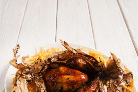 Baked chicken in paper cover, free space. Roasted poultry on white wooden background, copy space for text or advertisement. Junk fast food, american cuisine, fat, menu conceptの写真素材