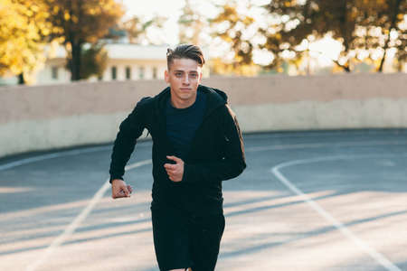 Young handsome man running down stadium track. Professional sprinter training for marathon. Sport, competition, persistence, goal, motivation conceptの写真素材