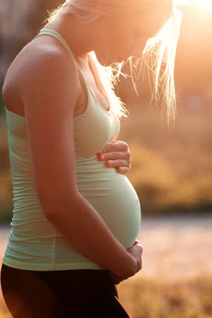 Profile of pregnant woman hugging her belly on sunset. Future mother holding her stomach with love. Pregnancy, maternity, family conceptの写真素材