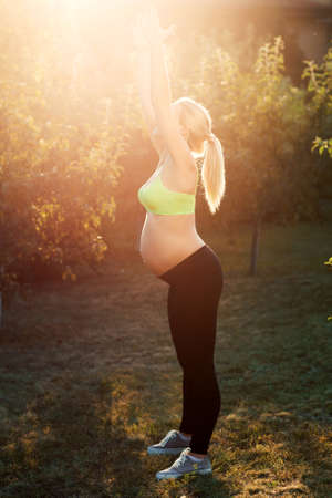 Pregnant woman stretching early in morning outdoor. Profile of young expectant female reaching for sun. Enjoy nature, peacefulness, relaxation, healthy pregnancy conceptの写真素材