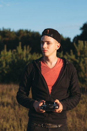 Young man standing with rc transmitter outdoor. Attractive guy attentively looking for piloting...