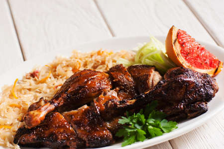 Grilled duck served with stewed cabbage and grapefruit slice. Tasty meal of brown roasted poultry with vegetable, white wooden background. Dining, appetizing, Christmas food conceptの写真素材