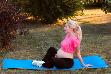 Side view on pregnant sitting in lotus pose. Expectant woman with naked belly practicing yoga at nature, meditation, relaxation, healthy pregnancy conceptの写真素材
