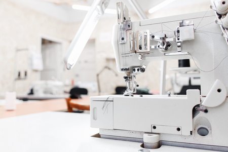 Professional garment factory office, free space. Sewing machine on foreground, blurred workroom for...