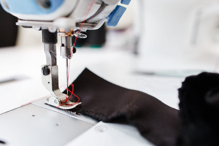 Sewing machine stitching dark fabric close-up. Detail photo of shuttle of needle working process. Garment industry, seamstress workplace, tailor workshop conceptの写真素材