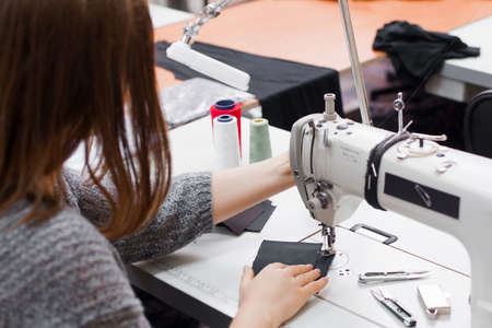 Seamstress sewing at machine, back view. Female tailor stitching material at workplace. Preparing fabric for clothes making. Tailoring, garment industry, designer workshop conceptの写真素材