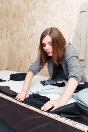 Young fashion designer measuring fabric, free space. Creative woman tailor preparing material for sewing cloth. Garment industry, tailoring process, pattern cutting conceptの写真素材
