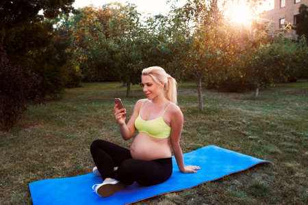 Smiling woman chatting on smartphone outdoor. Expectant female networking while resting at nature. Relax, pregnancy, communication conceptの写真素材