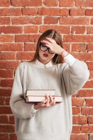 Stressed girl with books forgot something important. Desparate woman girl covering her face with hand. Stress, education, bad memory, tiredness conceptの写真素材