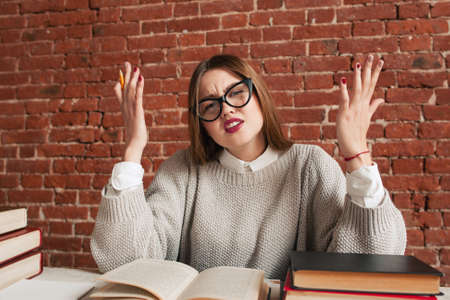 Silly student sitting at desk. Young beautiful woman in glasses trying to understand material, but doesnt get it. Stupid girl, ignorance, laziness conceptの写真素材