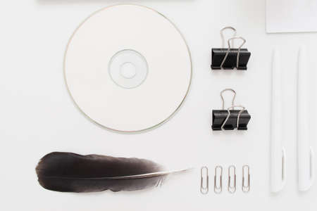 Cd with clips and feather on white flat lay. Top view on communication devices of different generations, free space. Art, business, creation, stationery, writing, memory, information, ordering conceptの写真素材