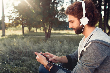 Profile of man in headphones using smartphone. Young guy choosing favorite music in mobile phone at...