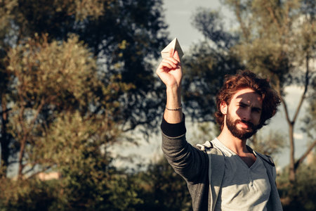 Paper airplane launching in park, free space, Man holding handmade paper airplane in hand, face in...
