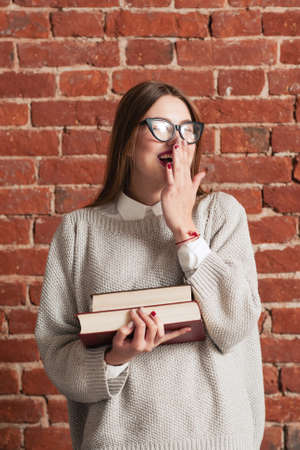 Student girl playfully laughing with books. Attractive woman covering her mouth with hand while enjoying funny joke. Coquette, flirt, fun, joy conceptの写真素材