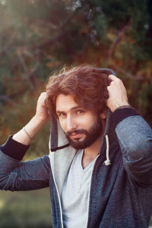 Portrait of attractive guy covering head, free space. Stylish man looking at camera,while hiding from wind, sunlight flare. Protection, healthcare, leisure conceptの写真素材