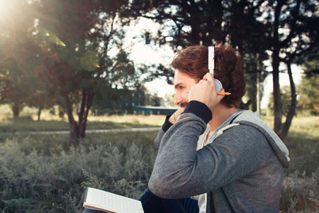 Man wearing headphones, relaxing at nature. Profile of young modern musician listening to music. Art, inspiration, creation, composition conceptの写真素材